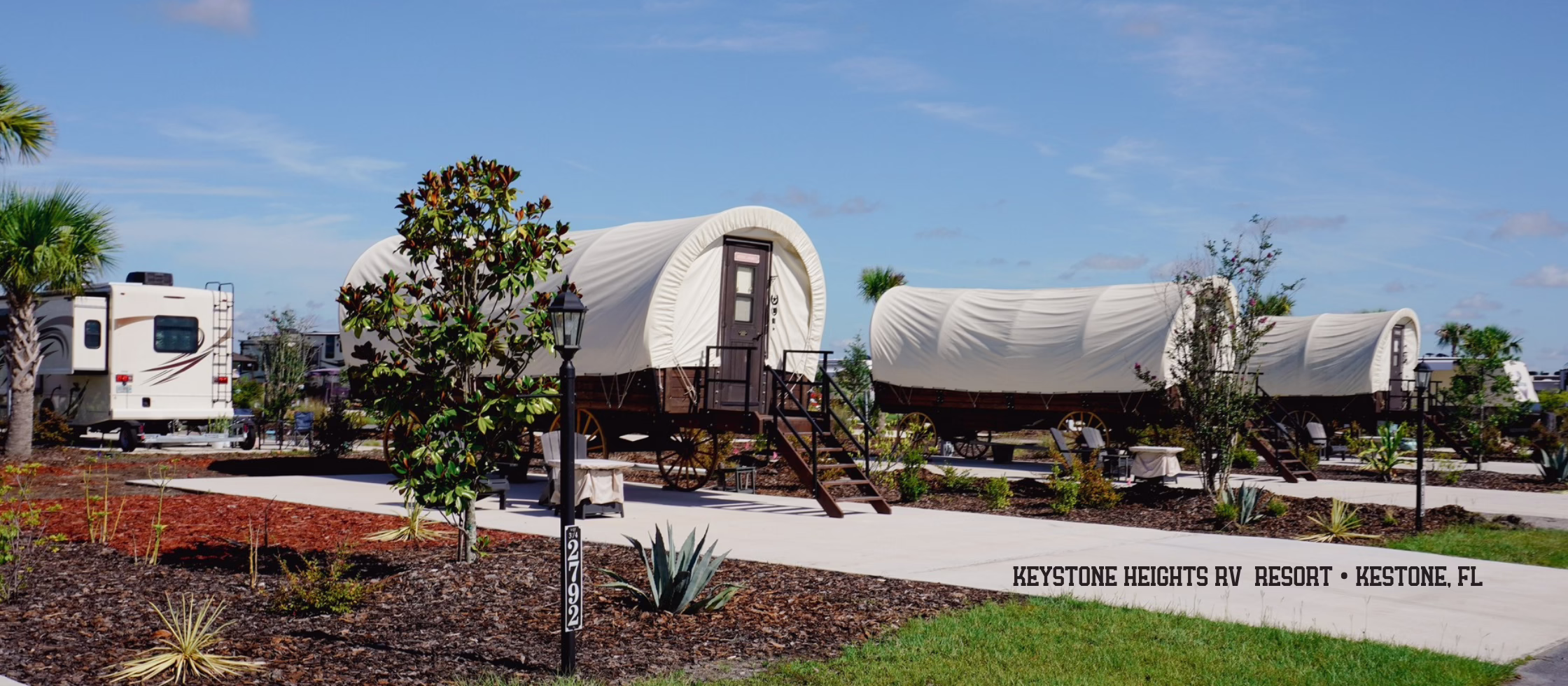 BLOG HEADER FOR - Campground industry trends 2026 showing covered wagon accommodations alongside traditional RV sites - 3 covered glamping wagons lined up on cement rv site pads at Keystone Heights RV Resort in Keystone, FL